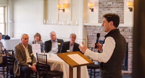 Man speaking to group at tables 