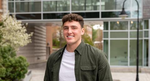 Accounting major Patrick Yudkin stands outside UNH Paul College in the courtyard, hands in his pockets, smiling at the camera.