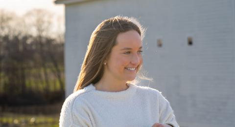 UNH accounting and finance major Reagan Calcari leans against a fence near the campus horse barns, smiling to someone off camera.