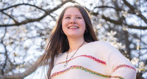 UNH marketing major Tiffany Marrotte stands in front of a blooming tree, hands on her hips, smiling, with the sun outlining her body.