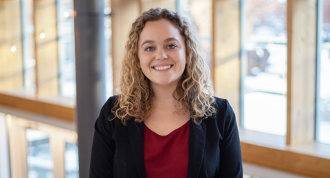A female student dressed in business attire smiles at the camera.
