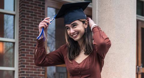 Hannah Donahue adjusts her graduation cap while sitting on steps at UNH campus.