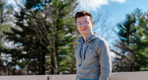 A male student leans against a railing with his hands in his pockets.