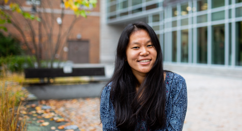 A female student sits in Paul College's outdoor courtyard, smiling at the camera.