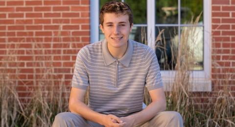 Brett Schultz smiles at the camera head on, seated with elbows on his knees