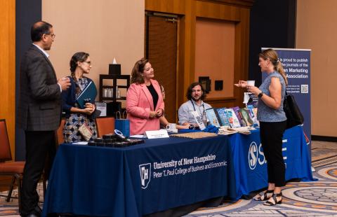 faculty talk to conference attendees from behind a UNH Paul college table