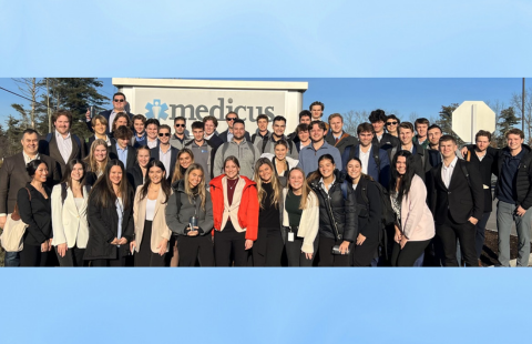 Students crowd for a group photo outside in front of a business sign for Medicus