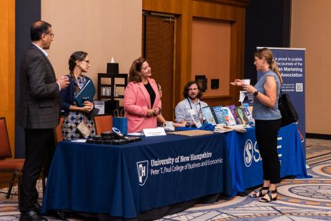 faculty talk to conference attendees from behind a UNH Paul college table