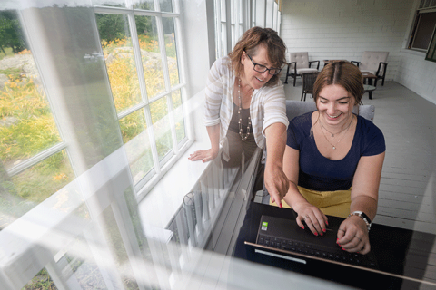A woman points over the shoulder of a student on a laptop