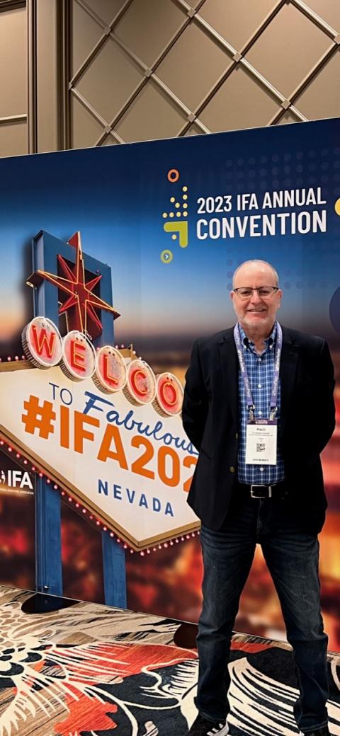 Dr. Aliouche in front of the conference banner