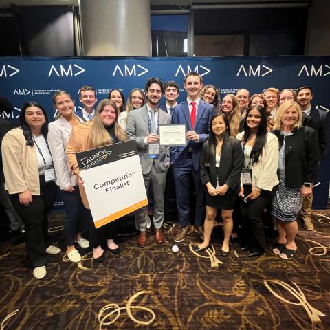 A large group of UNH Marketing majors gathers for a photo opportunity at the American Marketing Association's International Collegiate Competition. One student holds a sign that reads, "Competition finalist."