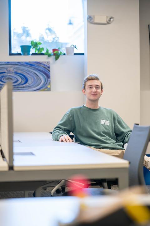 Marketing and Finance major Ian Lidster sits at a table in the UNH ECenter, smiling at the camera.