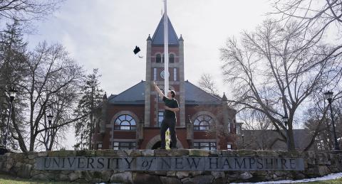 Diego Smith tosses his graduation cap into the air in celebration in front of thompson hall.