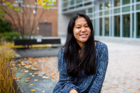 Sadie Mazzola '21 A female student sits in Paul College's outdoor courtyard, smiling at the camera.