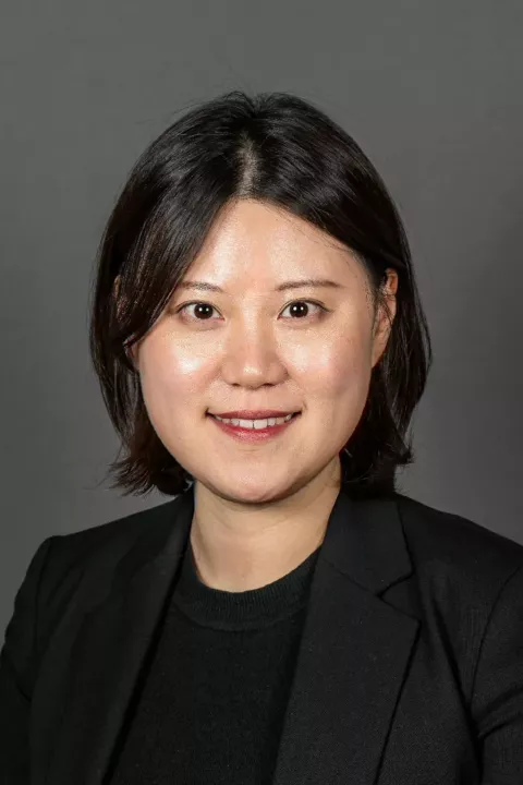 Headshot of Yoon Kang. She has dark hair that is shorter than her shoulders, and is wearing a black top and blazer.