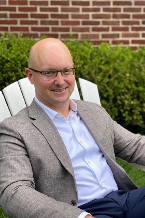 Andrew Earle sits in an Adirondack chair and smiles at the camera